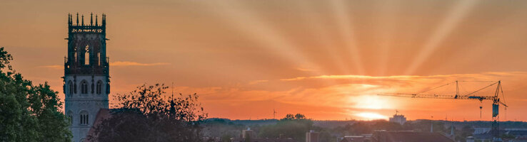 ATLANTIC Hotel Münster Skybar View Sunset over Münster with church tower, trees and a crane in the foreground.