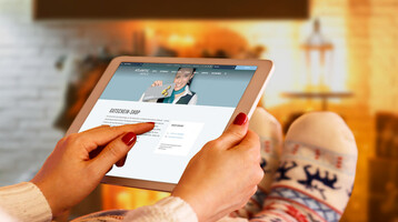 Voucher shop ATLANTIC Hotels Person relaxing in front of the fireplace with a tablet on which a hotel website is open. Room decorated for Christmas.