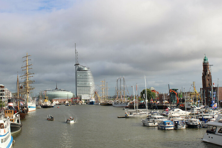 View at the ATLANTIC Hotel Sail City from the habour of Bremerhaven Harbor view with sailing ships, modern buildings and a lighthouse under a cloudy sky.