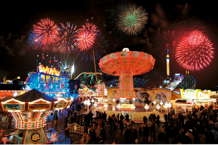 Bremer Freimarkt Night shot of a busy funfair with illuminated rides and colorful fireworks in the sky.