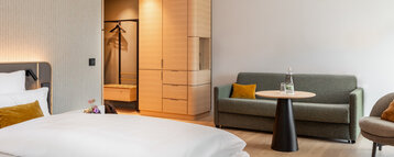 Blick auf das gemachte Bett und die Sitzecke mit Sofa und Sessel im barrierearmen Zimmer