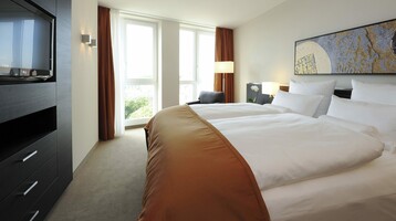 Room in the ATLANTIC Grand Hotel in Bremen Bright hotel room with large bed, modern decor, window with curtains, TV and artwork on the wall.