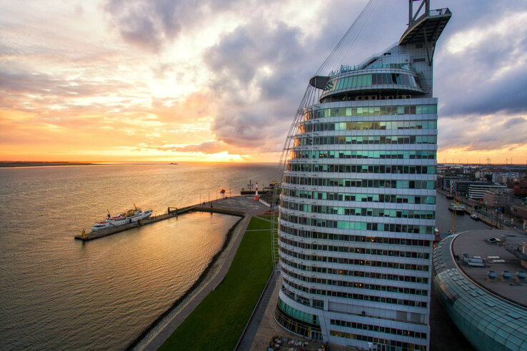 ATLANTIC Hotel Sail City – Exterior view ATLANTIC Hotel Sail City in Bremerhaven, at sunset on the waterfront, with modern, curved glass design.