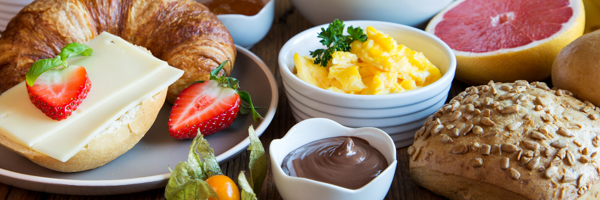 Nahaufnahme eines Frühstückstisches mit Früchten, Brötchen, Croissant, Rührei und Aufstrichen