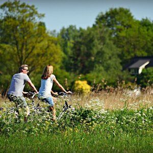 Bicycle rental at the ATLANTIC Hotel Landgut Horn A couple rides a bicycle through a green meadow in front of a house in the background.