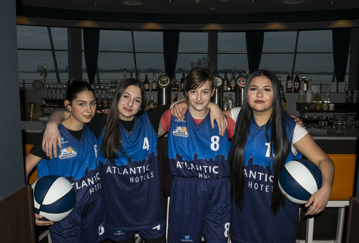 Team picture of the Eisbären Bremerhaven U14 girls' team Four young basketball players in blue jerseys pose smiling in a hotel bar.