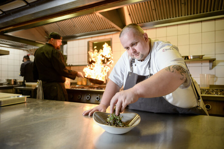 Kitchen of the CAMPUS restaurant Chef at the ATLANTIC Hotel Universum prepares a dish while flambéing takes place in the background.