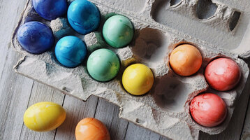 Oster-Angebot mit Übernachtungen im ATLANTIC Hotel Münster Bunte, gefärbte Ostereier in einer Eierkartonverpackung auf Holzoberfläche.